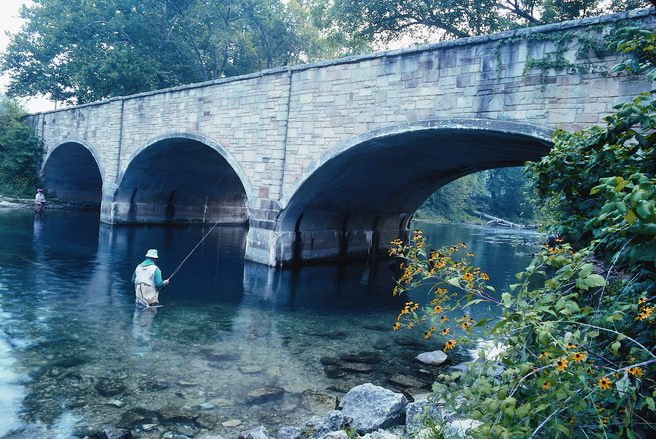 a man in a river fishing underneath a bridge