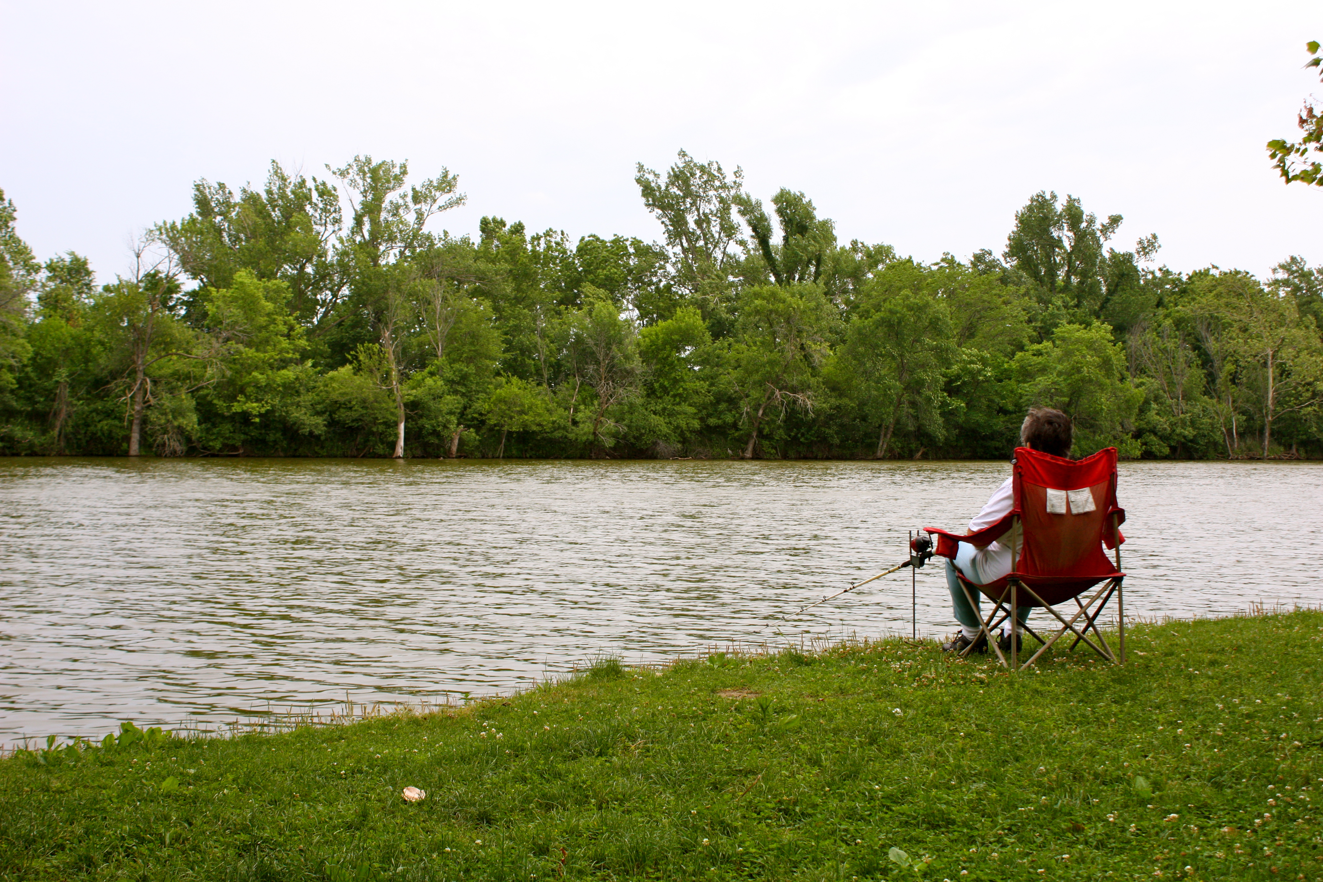 a person sitting in a red chair fishing into a lake