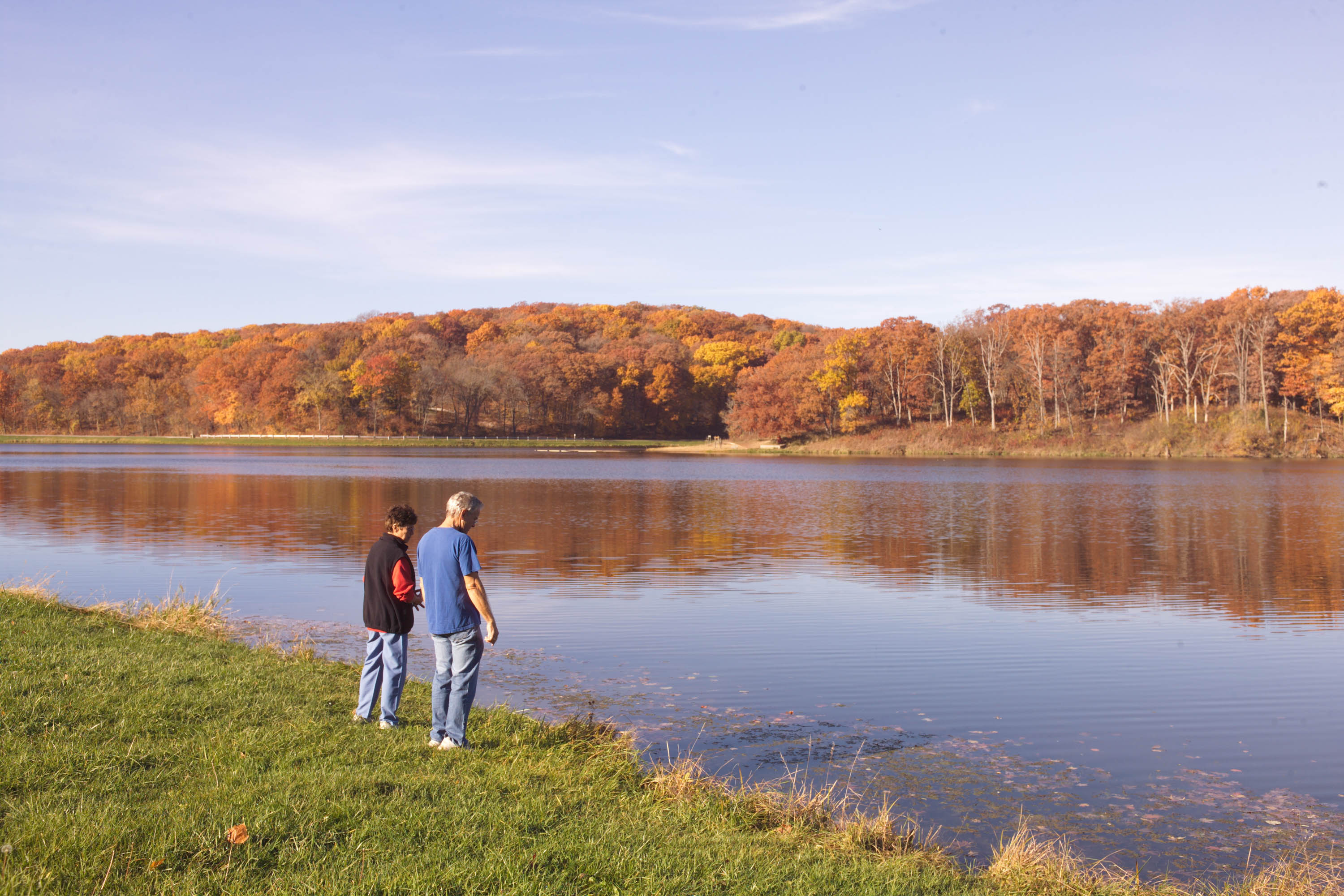 two people looking over a body of water surrounded by orange and yellow trees