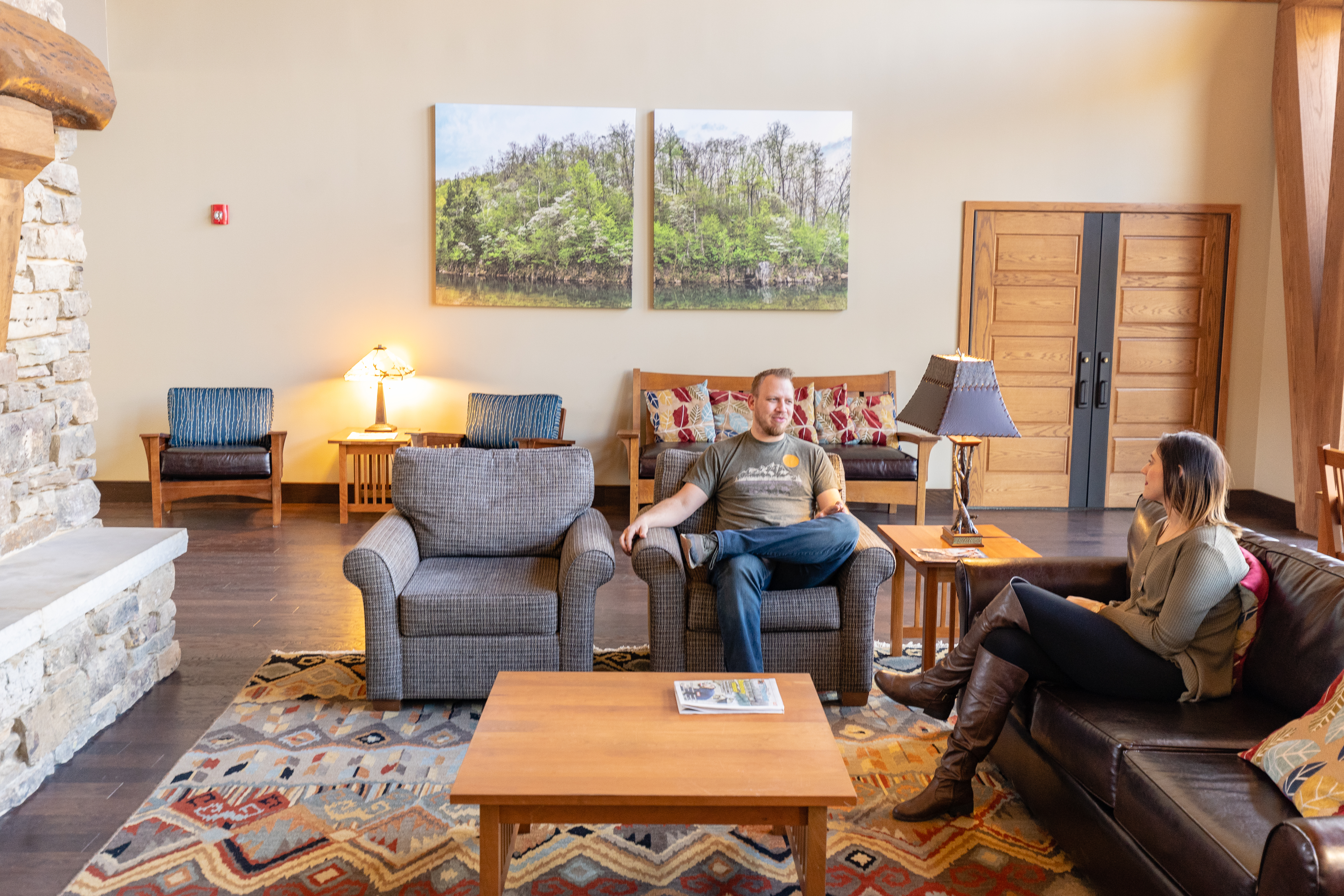 two people sitting in a lounge area in front of a large stone fireplace
