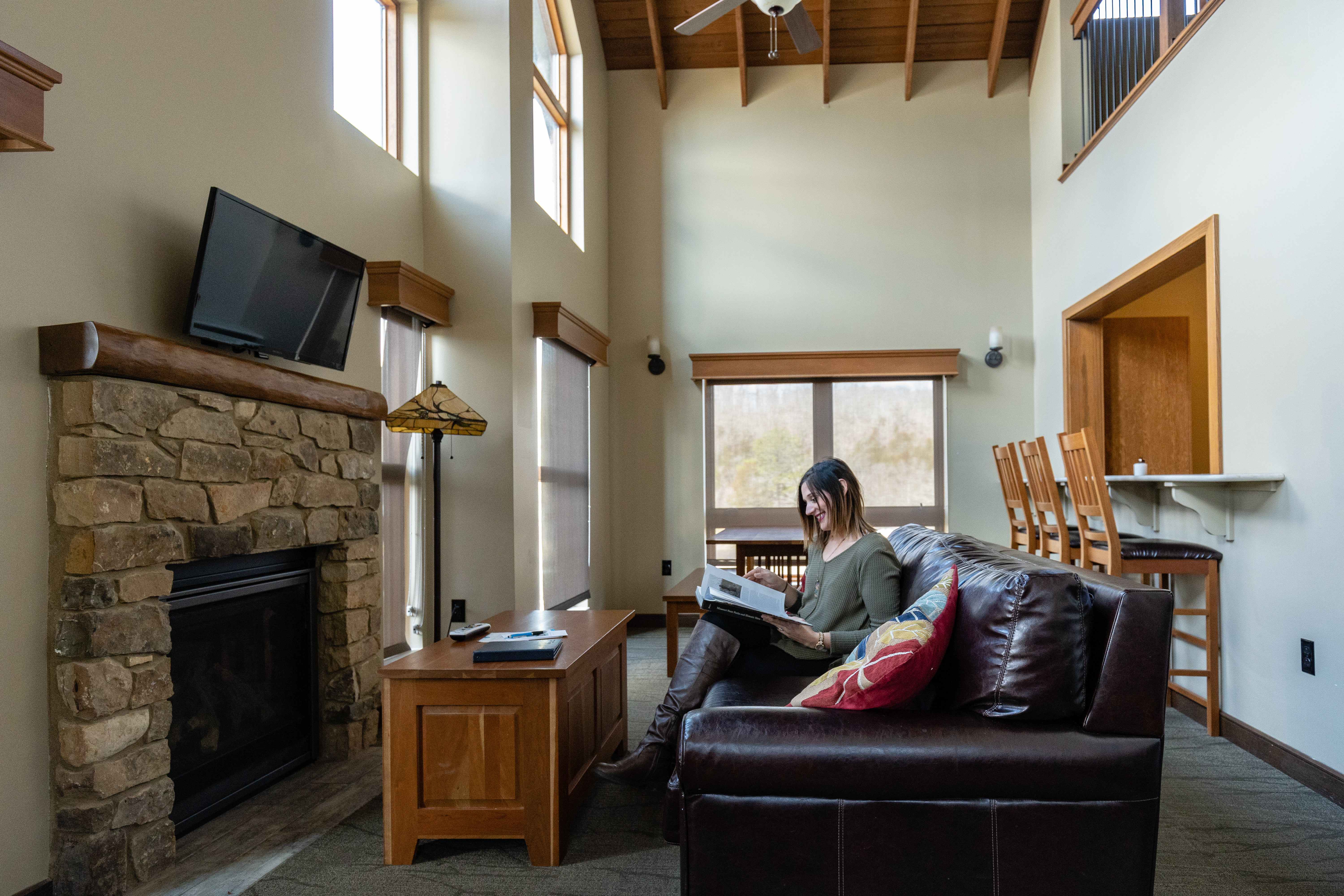 a woman sitting on a sofa reading a magazine in front of a stone fireplace