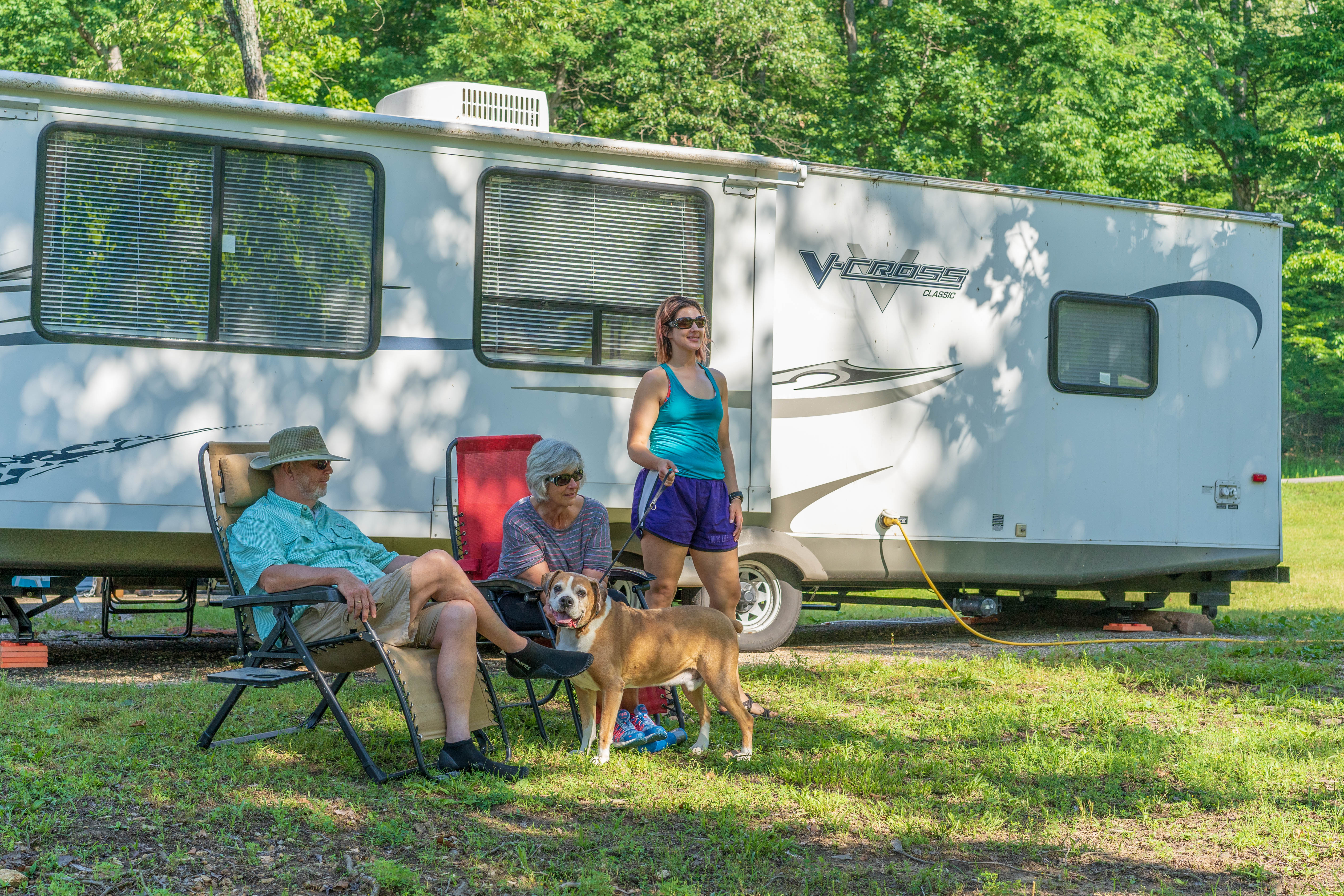 People sitting by a camper with a dog