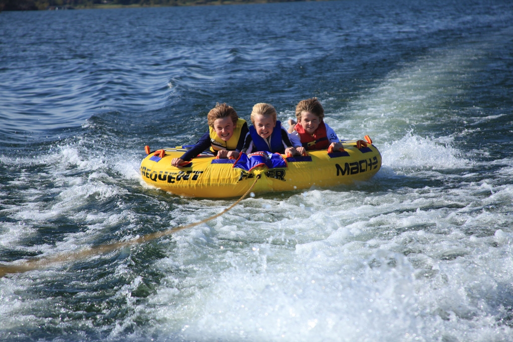 Three kids on an inflatable boat being pulled by a motor boat
