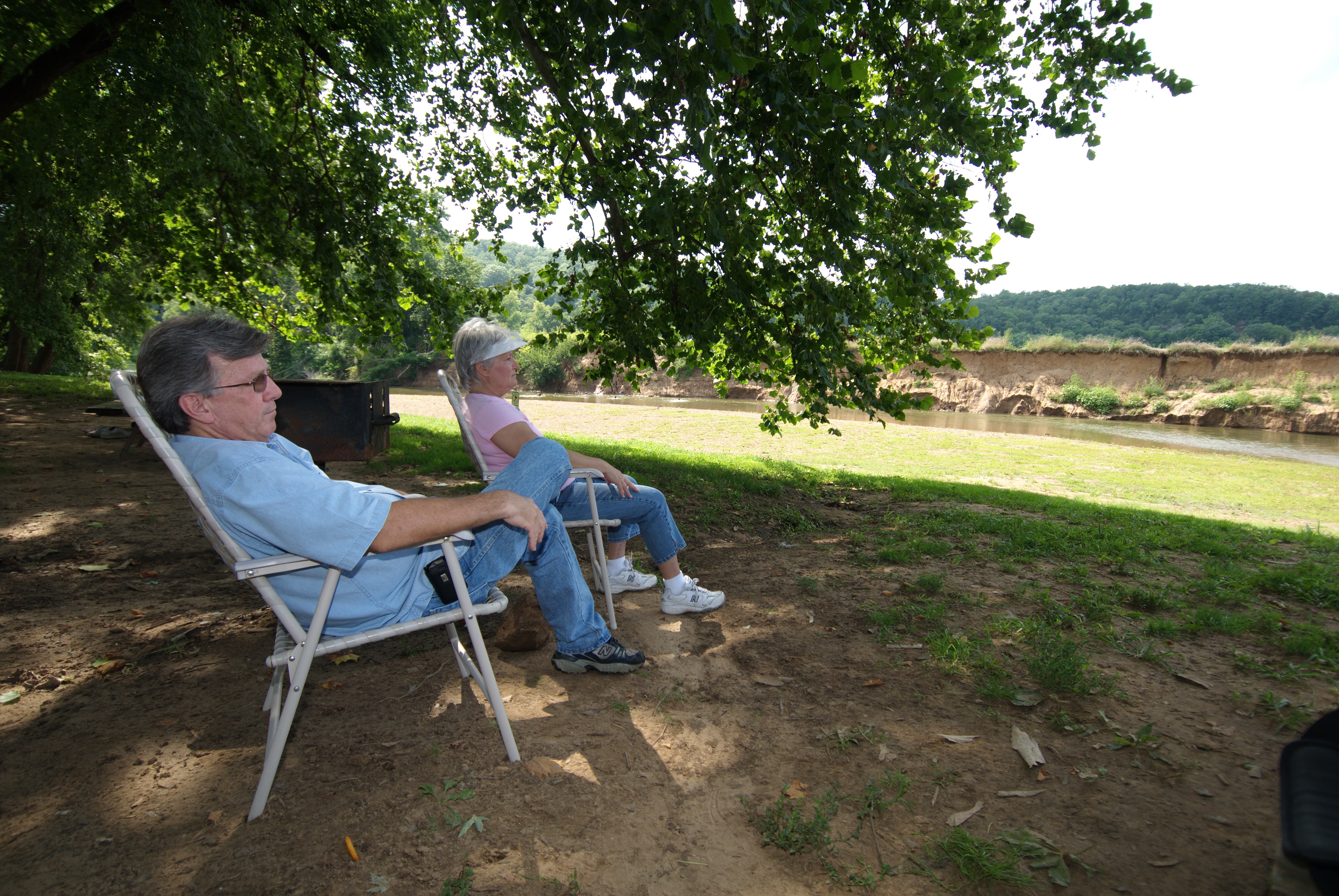Two people sitting in lawnchairs under a tree