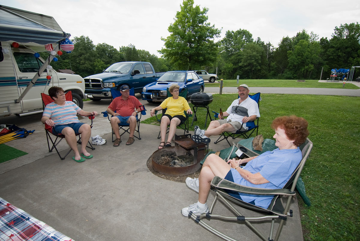 Five people sitting in lawn chairs around a fire pit outside a camper
