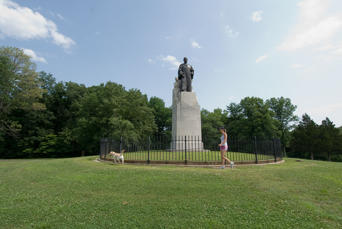 A woman walking a dog by the Dr. Edmund A. Babler Memorial Statue