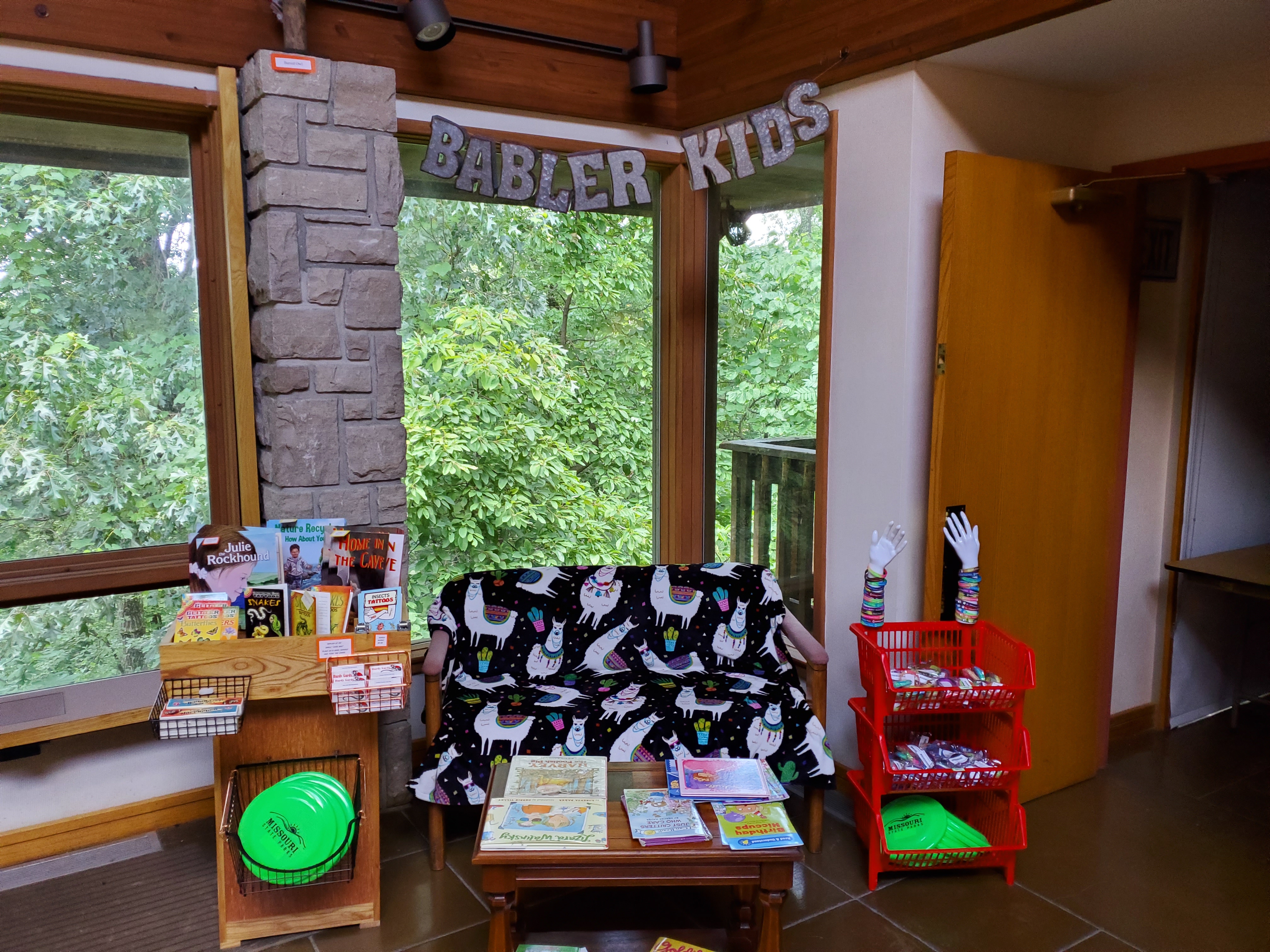 A couch and book shelf in a corner with &quot;Babler Kids&quot; on a sign above it