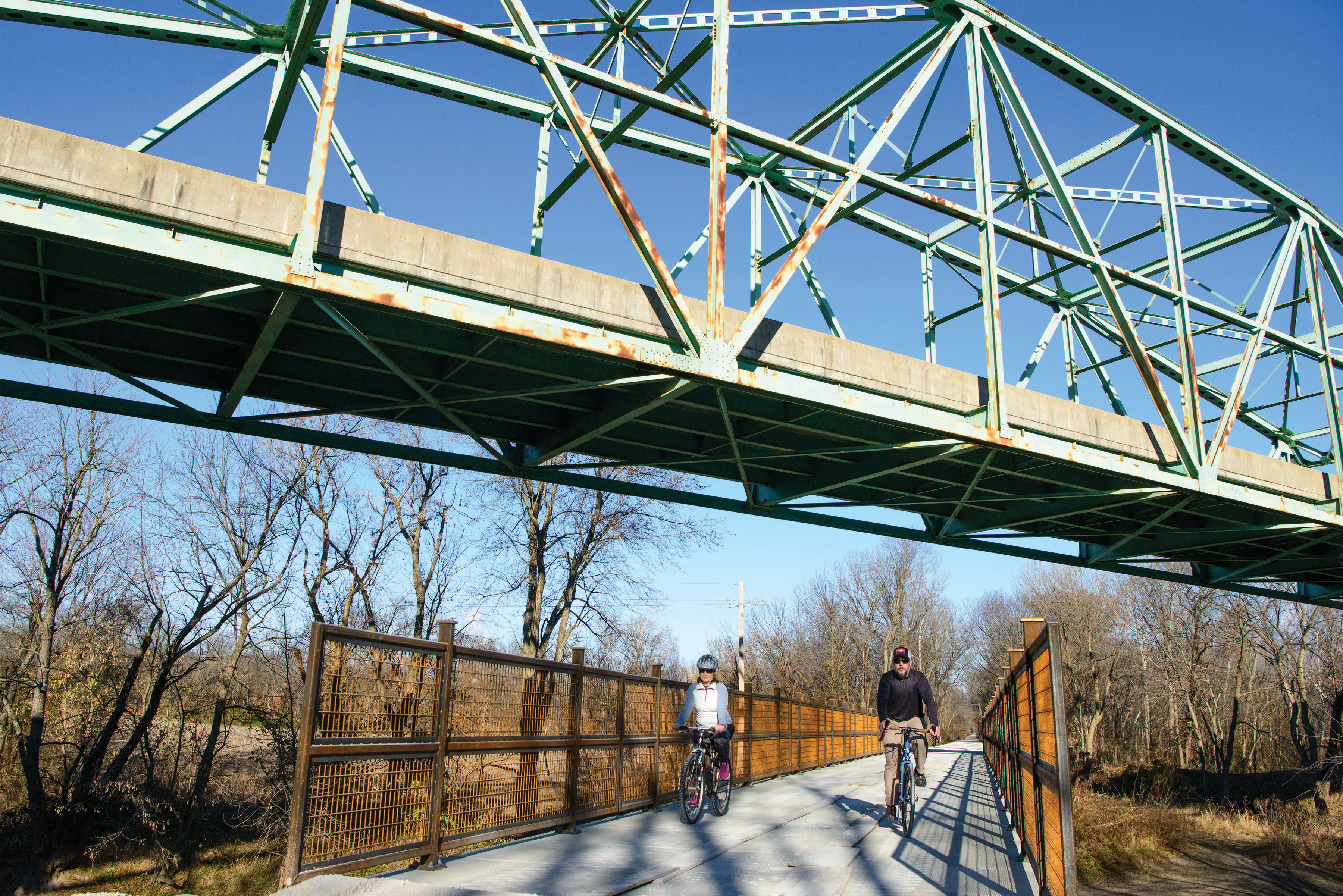 Two people biking under a bridge