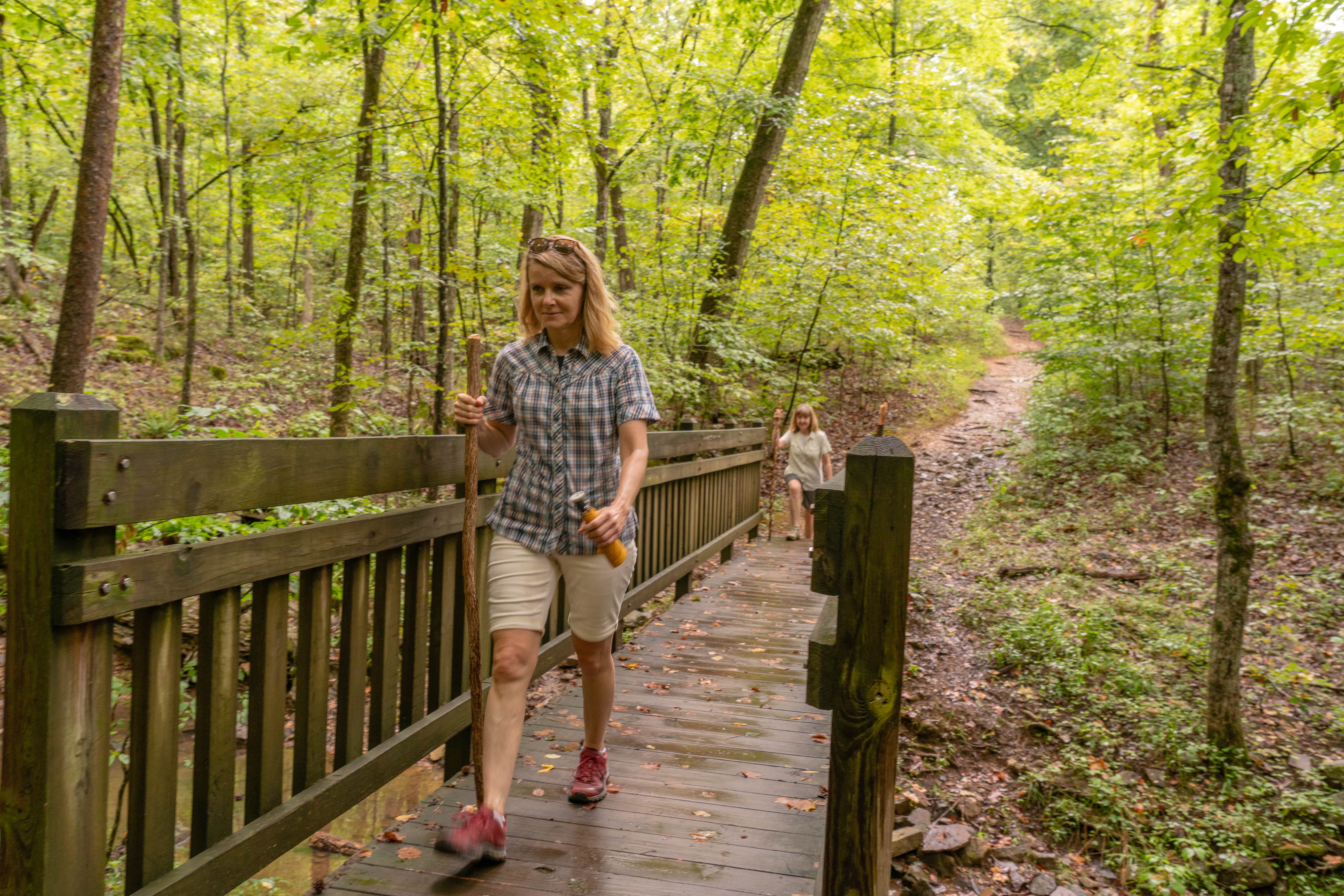 Two people walking across wooden bridge on a trail through the woods.