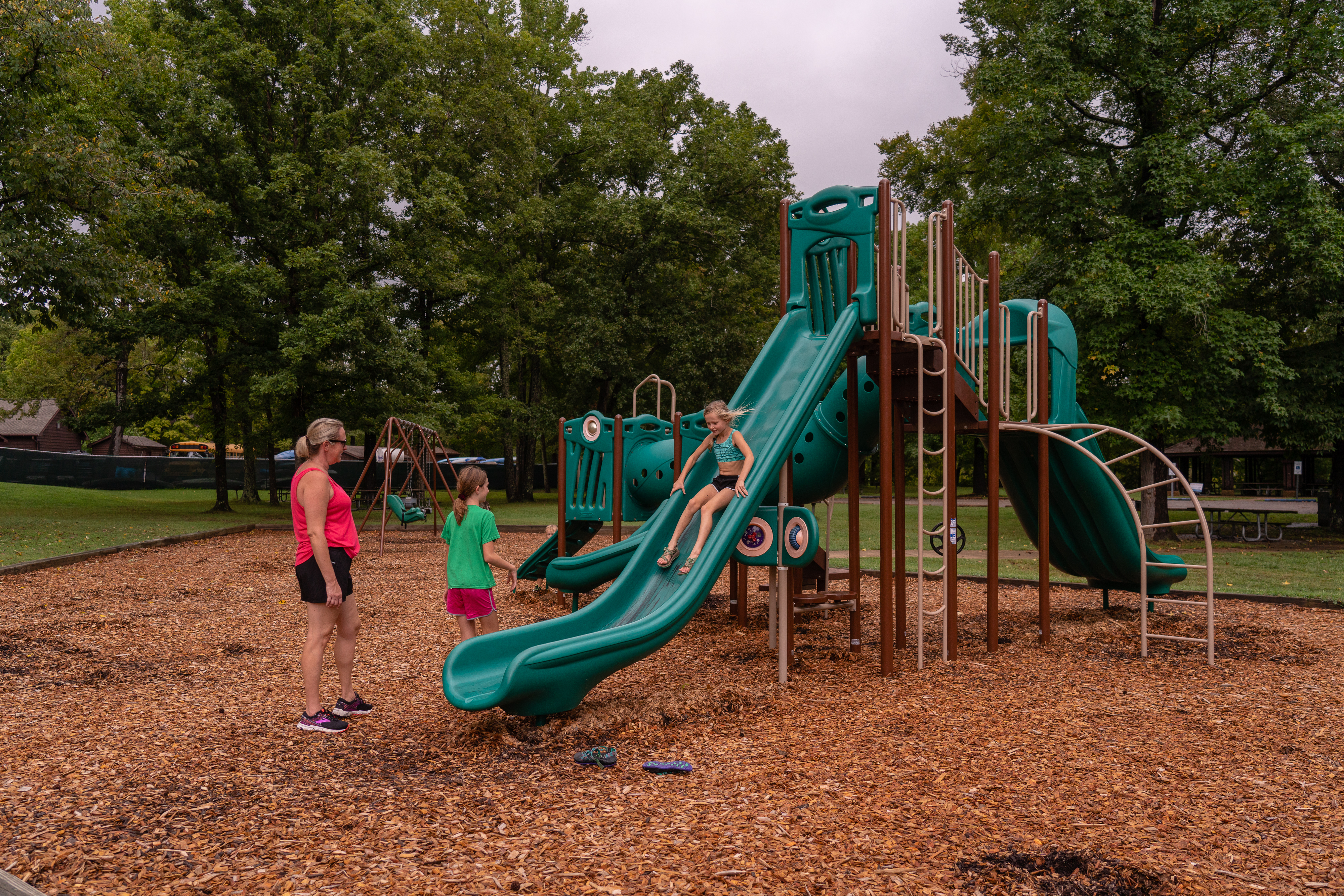 Playground equipment with a child sliding and an adult and another child watching.