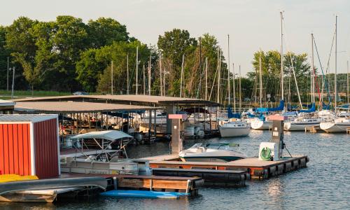 Sailboats, motorized fishing boats, a pontoon boat, a personal watercraft and a canoe docked at the marina boat slips on a sunny day