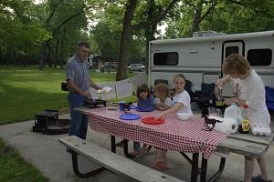 A family eating at a picnic table outside a camper