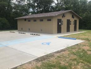 Exterior of showerhouse shows three showers and accessible parking spot