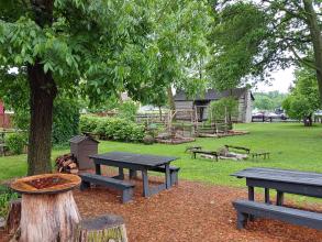 2 picnic tables and a chessboard on woodchips with a campfire and shelter in the background