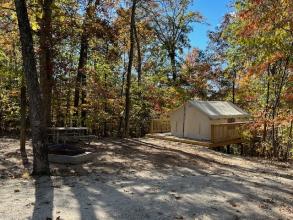 A closed beige-colored canvas tent sits on a wooden deck in a sloping area
