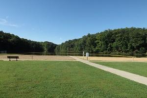 level grassy area with sidewalk leading to the beach and a bench