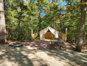 An open beige-colored tent sits on a wooden platform in a shady area