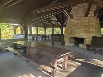 Wooden picnic tables and stone fireplace under the roof of the open shelter