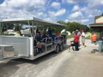 Senior citizens sitting in and standing outside of a stationary open-air tram on the Katy Trail