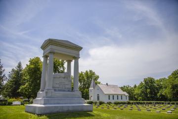 Monument in cemetery with green grass and chapel in the background.