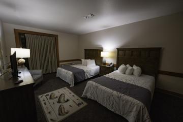 Room with two queen size beds, tables and lamps.