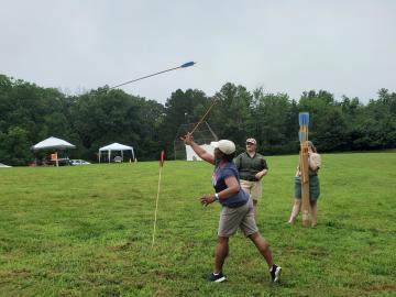A woman in a field using an atlatl