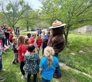 Children and adults gather around a person dressed up as Smokey Bear