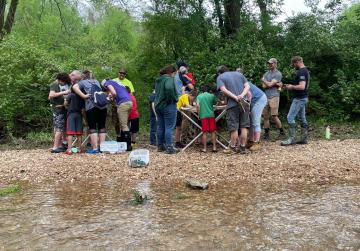 Children and adults gather around two popup stations set up on a creek bank