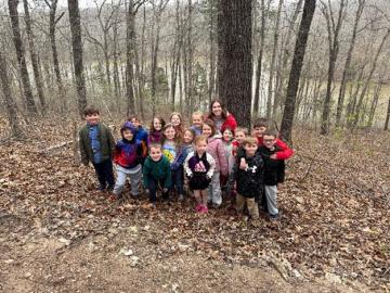 Students and a teacher pose for a photo in the woods with a river in the background