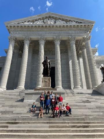 Students sit and stand on the outside steps of the Capitol in front of a statue of Thomas Jefferson
