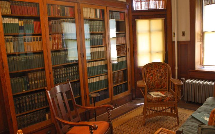 A home library with many books on shelves with glass doors and two chairs in front of them