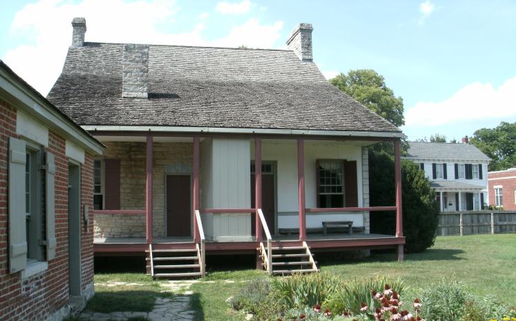A historic home made of white brick and white siding with a red shed in the backyard