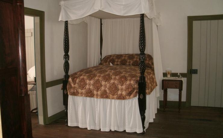 A bedroom with a small bed with black posts and a white canopy over it
