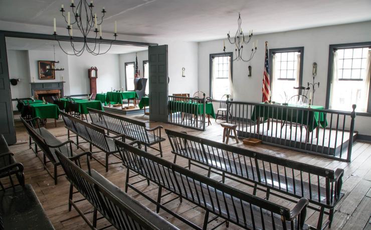 A meeting room with wooden benches and tables with green tablecloths