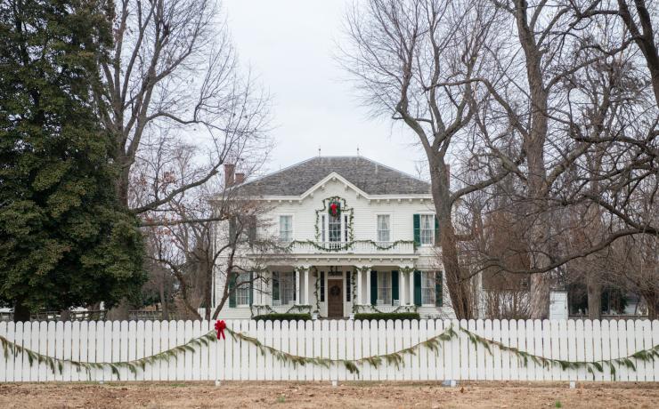 A white building behind a white fence, decorated with christmas wreaths