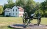 A civil war cannon with a white house behind it