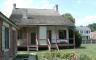 A historic home made of white brick and white siding with a red shed in the backyard