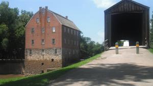 View of an old mill brom a near by walking path with a covered bridge