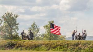 People setting off two cannons next to the American Flag