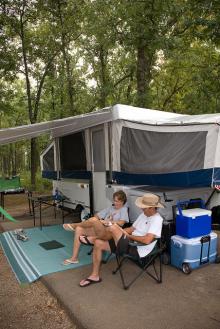two people sitting outside their camper reading