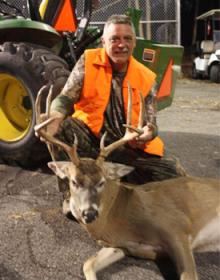 A hunter posing with a deer in front of a tractor