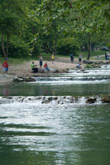 small cascades of water flowing down the river with people fishing on the bank