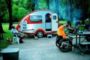 Man in wheel chair cooking over a camp stove with camper and another man in background