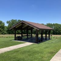 Open picnic shelter with roof and six picnic tables and a pedestal grill
